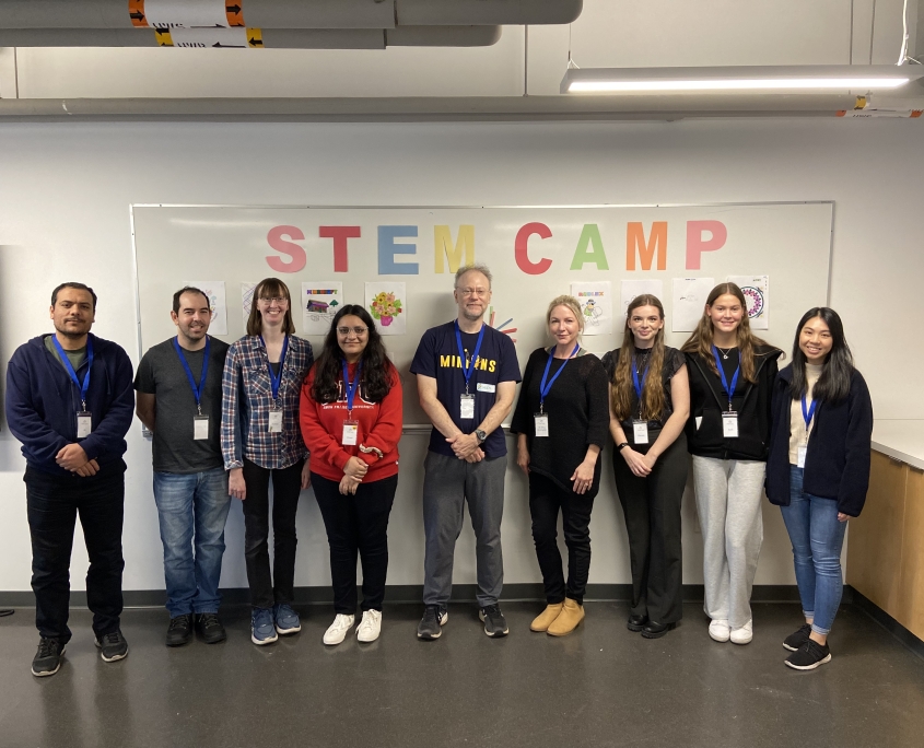 SFU STEM Camp, Fall 2023. Ali, Ivan, Siobhan, Chris Kerslake, Dr. Elina Birmingham, Meryssa Waite, Sarah, and Marissa standing in front of whiteboard at SFU Burnaby.